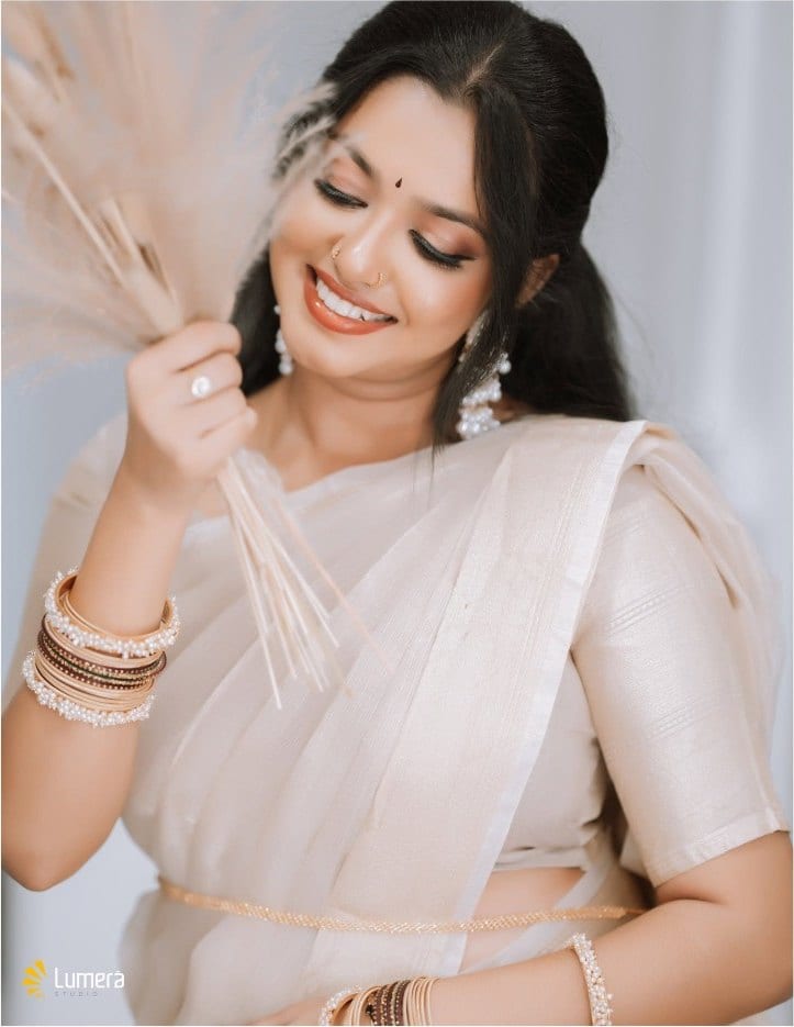 Portrait of a woman in a cream saree and pearl jewellery, smiling with dried flowers, photographed by Lumera Studio