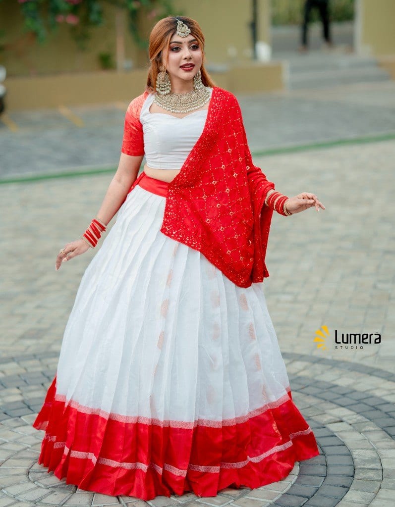 Full-length portrait in a red and white lehenga with gold jewellery, photographed outdoors by Lumera Studio