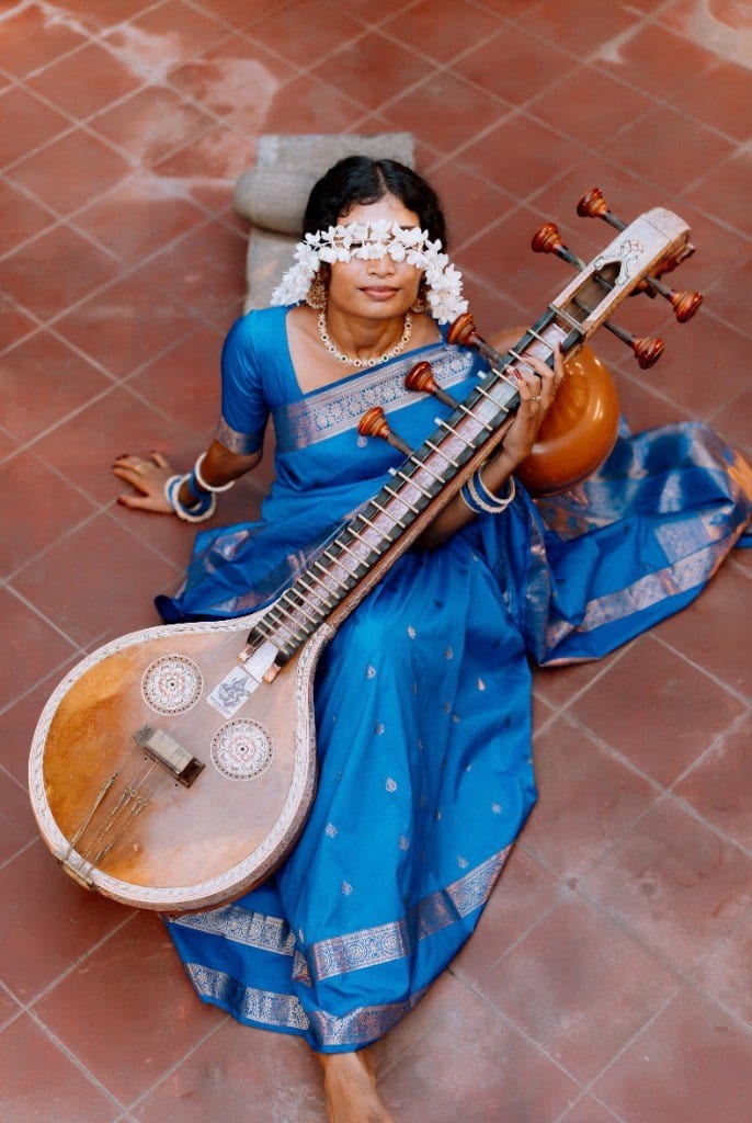 Woman in a blue saree seated with a veena, flowers across her eyes, photographed by Lumera Studio