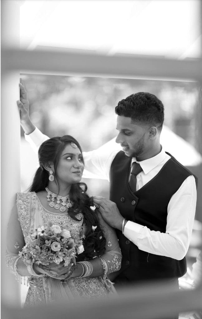 Bride in an embroidered lehenga holding a bouquet, standing with the groom in a black waistcoat, photographed by Lumera Studio